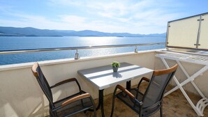 A balcony with a table and chairs, overlooking a body of water and distant mountains.