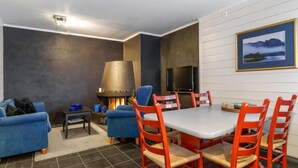 Una sala de estar acogedora con chimenea, televisión y un comedor con sillas rojas y una mesa blanca.