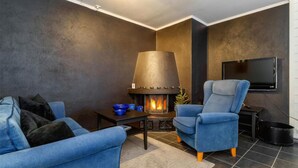 Una sala de estar moderna con chimenea, sillones azules, una mesa de centro y un televisor montado en la pared.