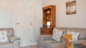 Un salon avec un canapé gris, un fauteuil assorti, un meuble en bois et une lampe fixée au mur.