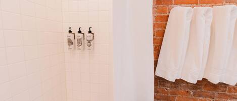 A bathroom with white tiled walls, a brick wall, and three bottles of hand soap on the wall.
