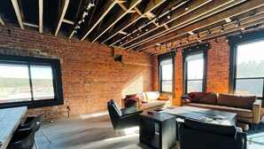 A spacious room with exposed wooden beams, a brick wall, and large windows offering a view of the outdoors. - The Timberline (Leadville)