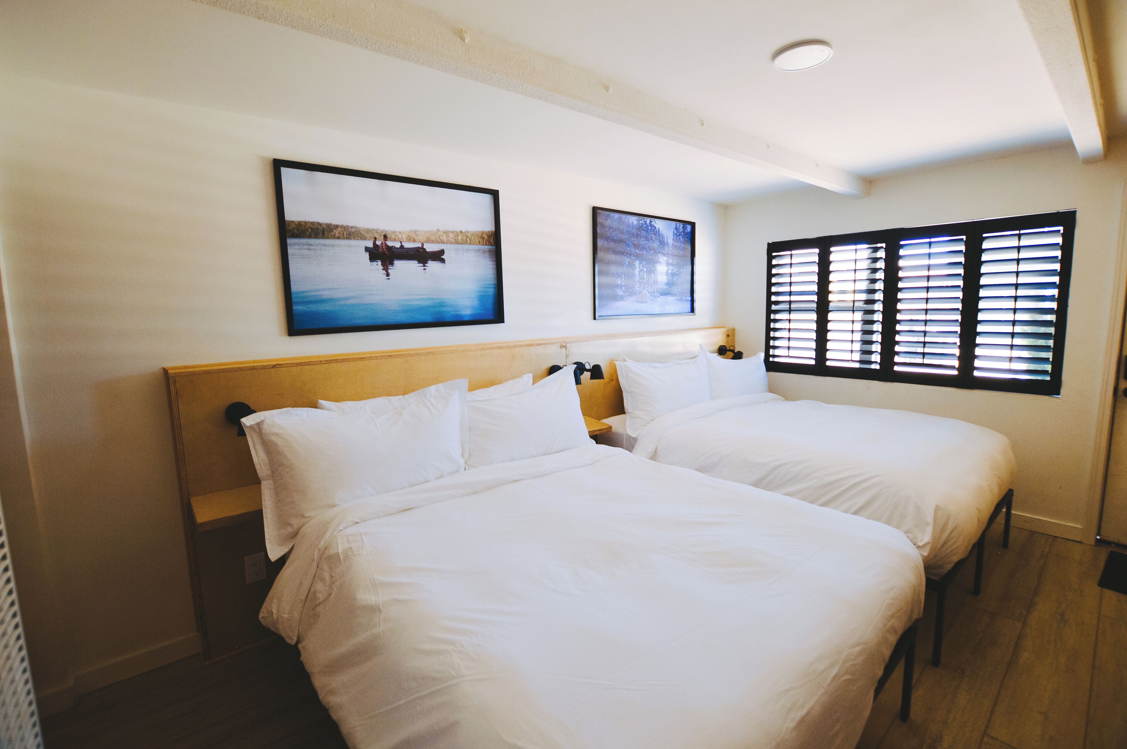 Quarto de hotel com duas camas, uma cabeceira de madeira e dois quadros na parede.