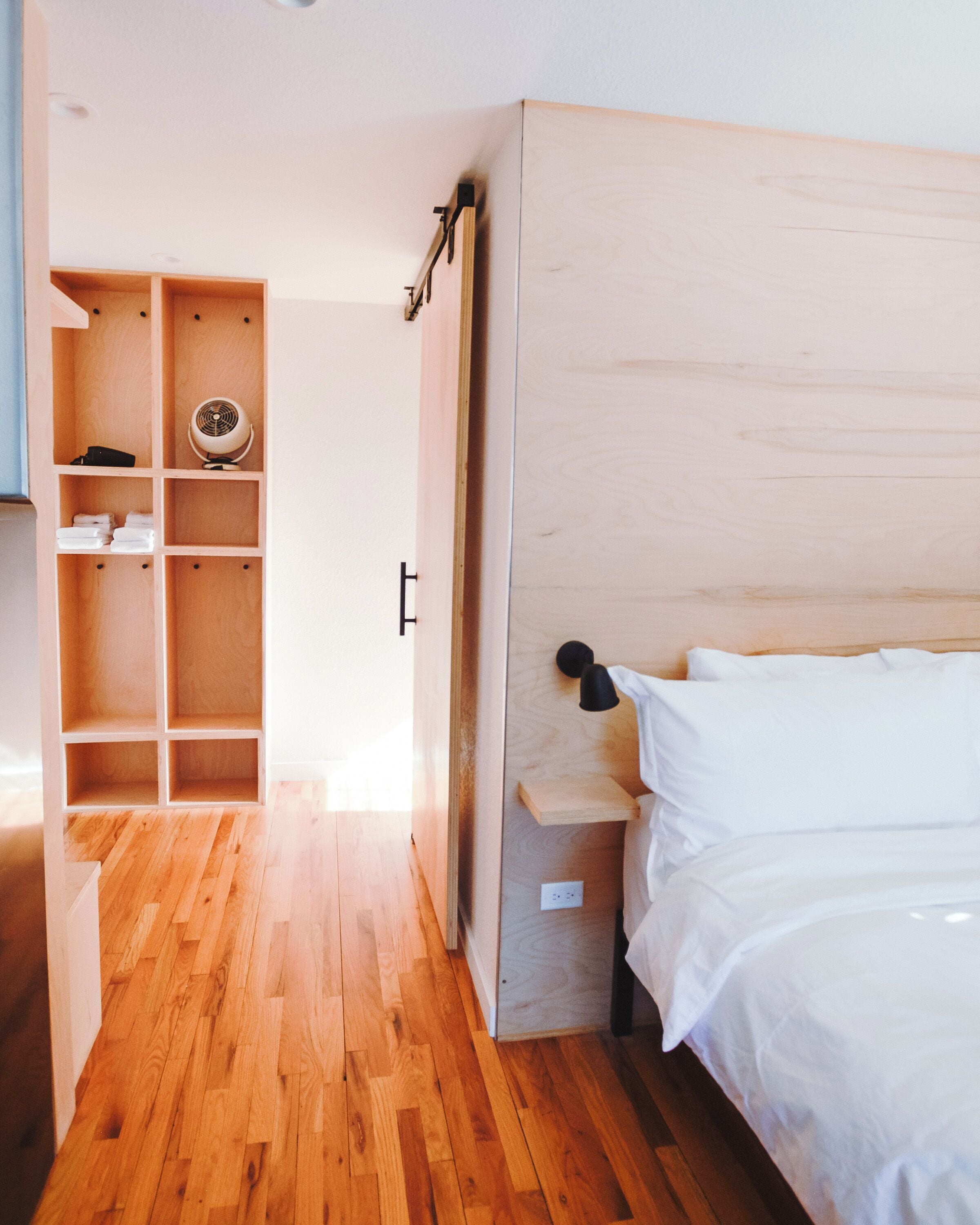 Quarto com cama de madeira, mesa de cabeceira, estante e guarda-roupa.