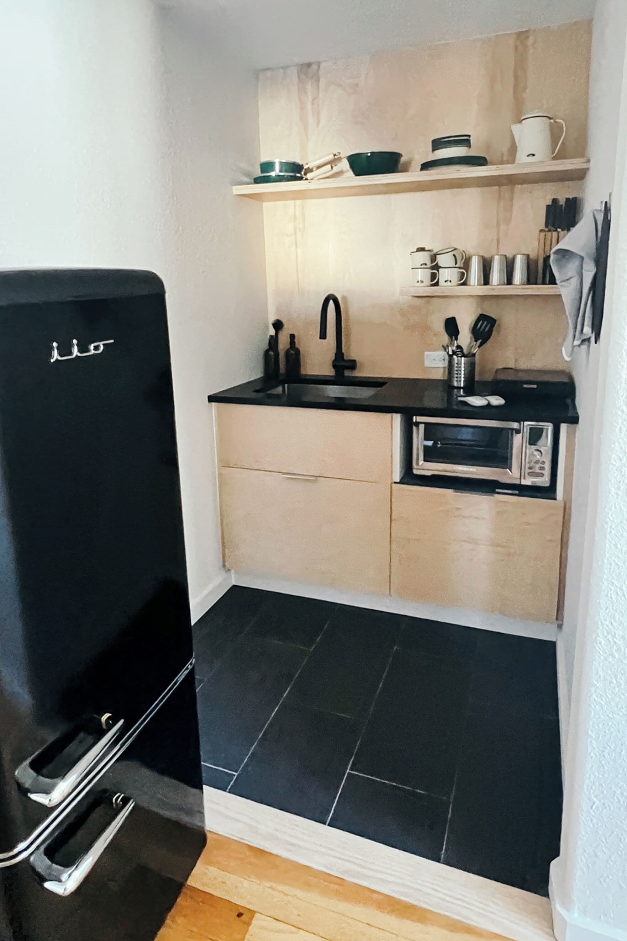 A compact kitchen with a black refrigerator, a microwave, and a sink.