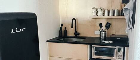 A compact kitchen with a black refrigerator, a microwave, and a sink.