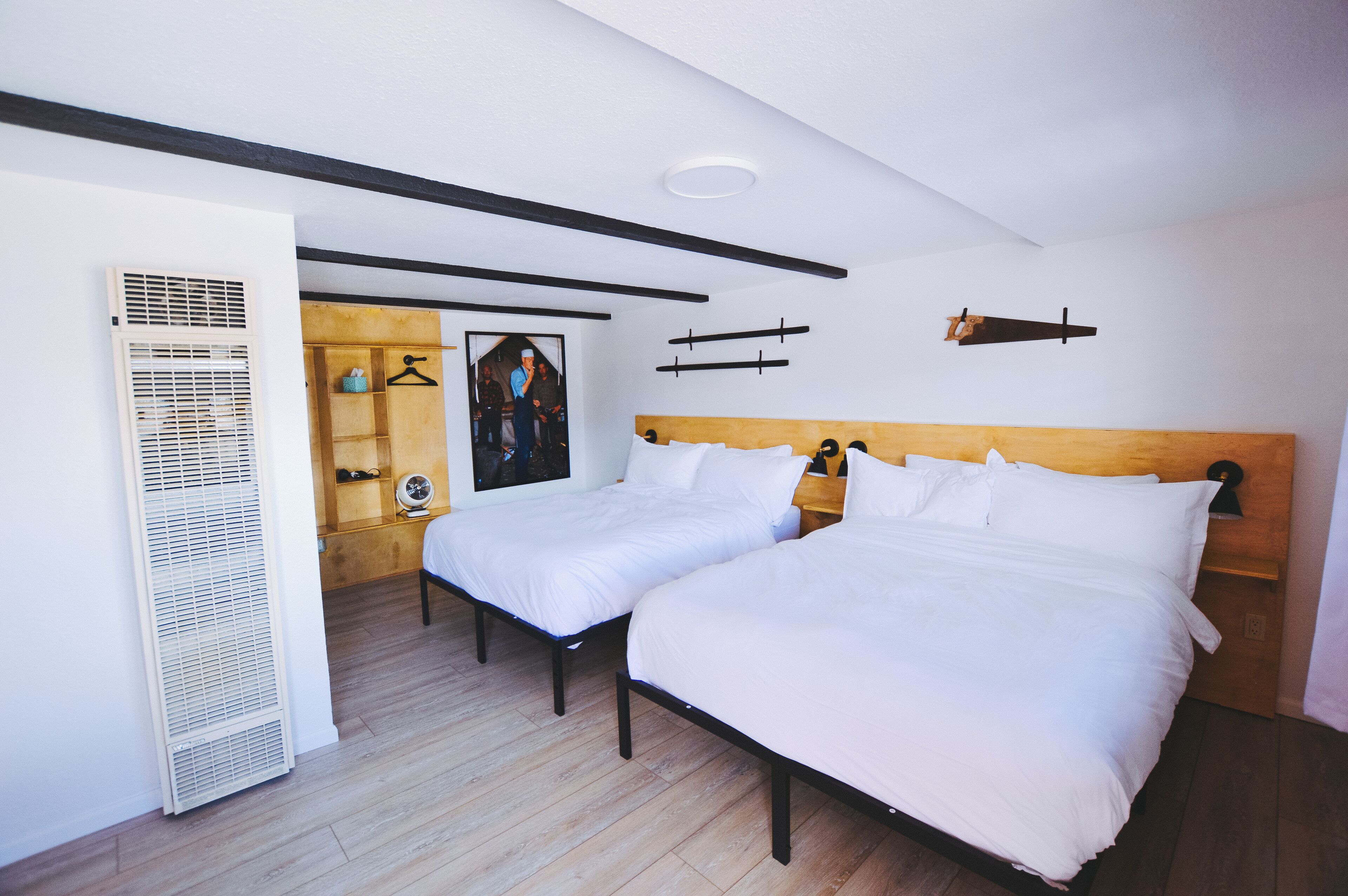 A room with two beds, a wooden headboard, a white radiator, and a framed picture on the wall.
