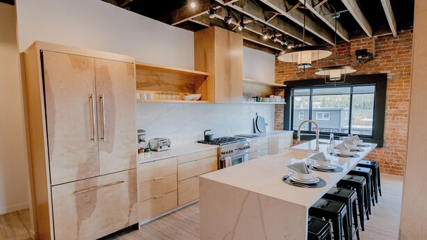 A modern kitchen with wooden cabinets, a central island, and bar stools. - The Timberline (Leadville)