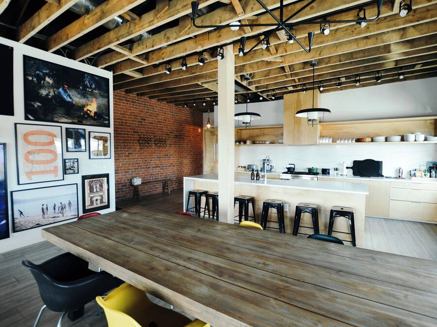 A modern kitchen with a brick wall, wooden ceiling beams, and a bar area with stools.