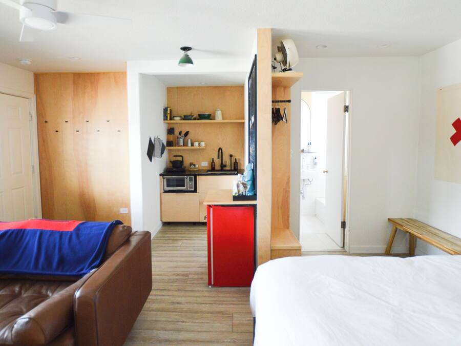 A compact hotel room with a kitchenette, a bed, a small seating area, and a bathroom.