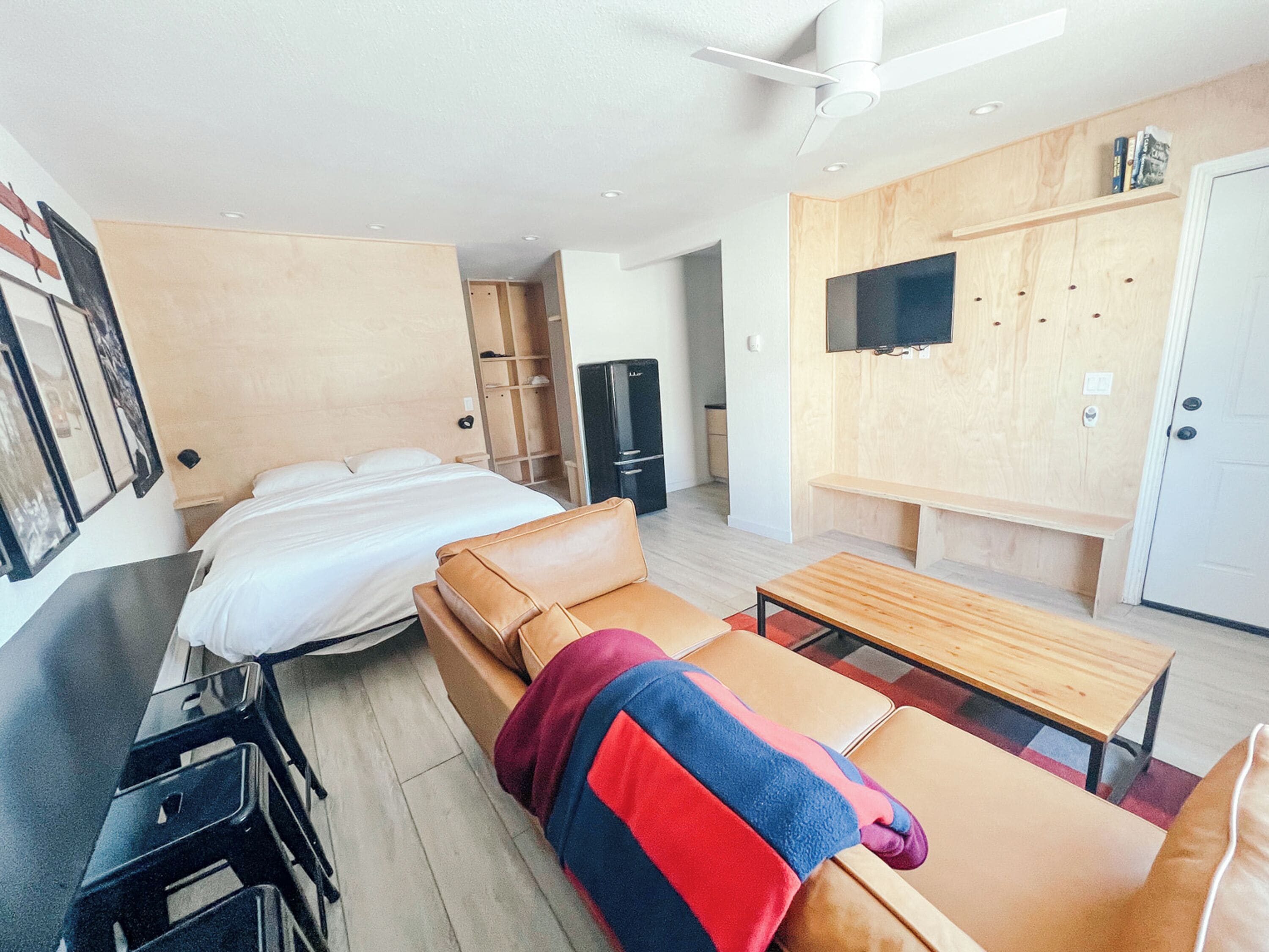 A modern hotel room with a bed, a sofa, a desk, and a TV mounted on the wall.