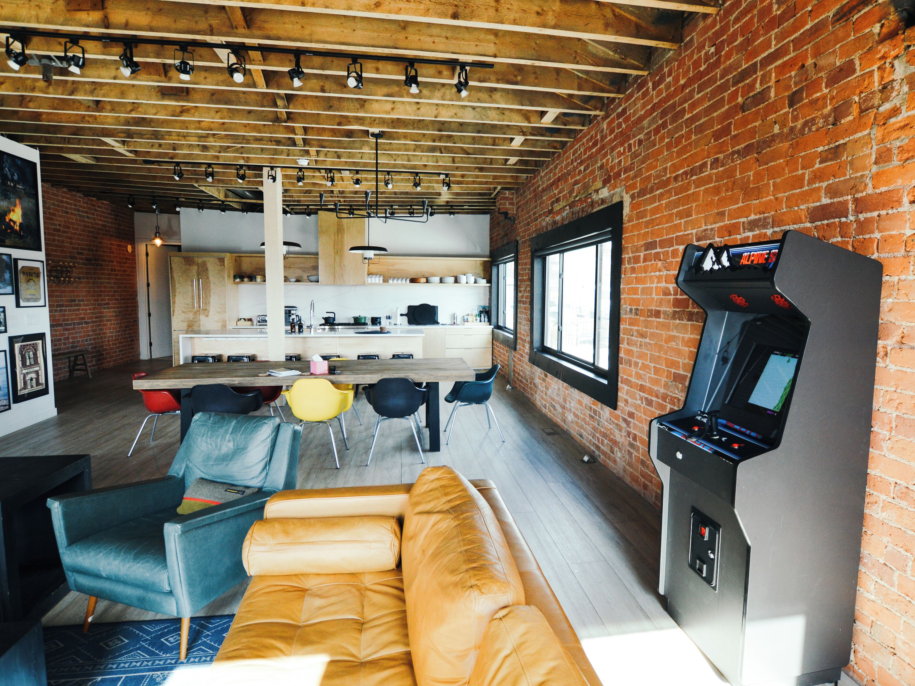 A modern kitchen with a dining area, featuring a sofa, chairs, and a gaming console.