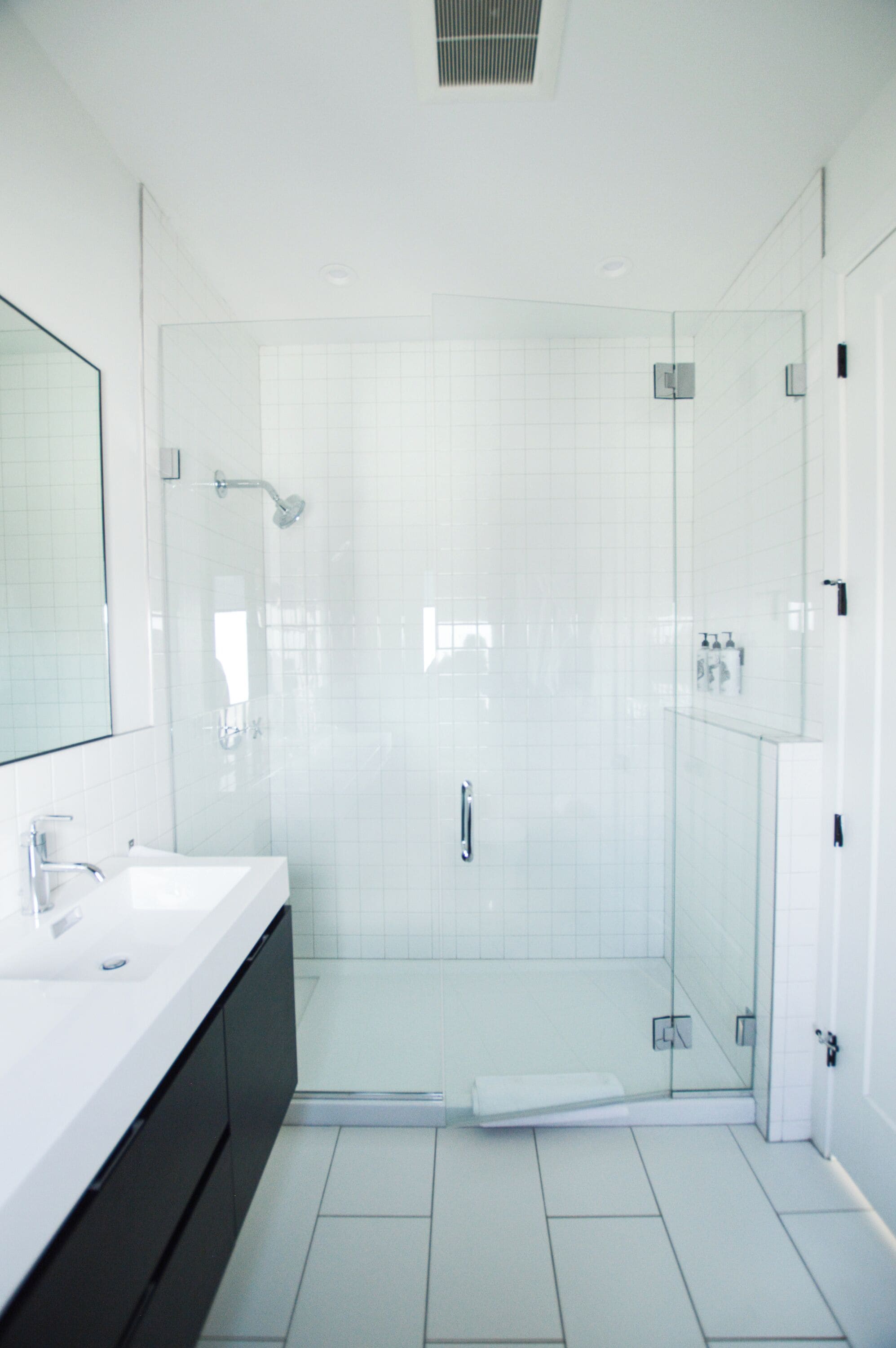 Un baño moderno con ducha acristalada, lavamanos blanco y un espejo grande.