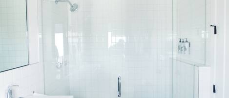 Un baño moderno con ducha acristalada, lavamanos blanco y un espejo grande.