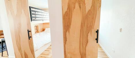 A room with a bunk bed, wooden sliding doors, and a wooden floor.