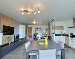A modern kitchen with a dining area, featuring a large table, built-in appliances, and a TV mounted on the wall.