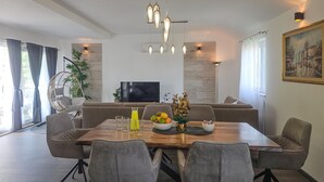 A modern dining area with a wooden table, grey upholstered chairs, and a television in the background.