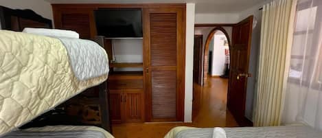 A hotel room with two beds, a television, a wooden wardrobe, and a bathroom visible through an archway.
