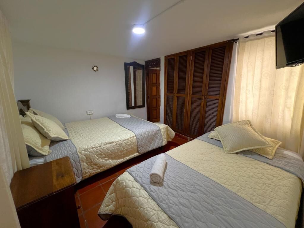 A room with two beds, a television mounted on the wall, and a wooden wardrobe.