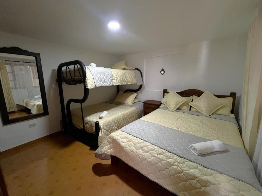 A hotel room with two beds, a bunk bed, a mirror, and a bedside table.
