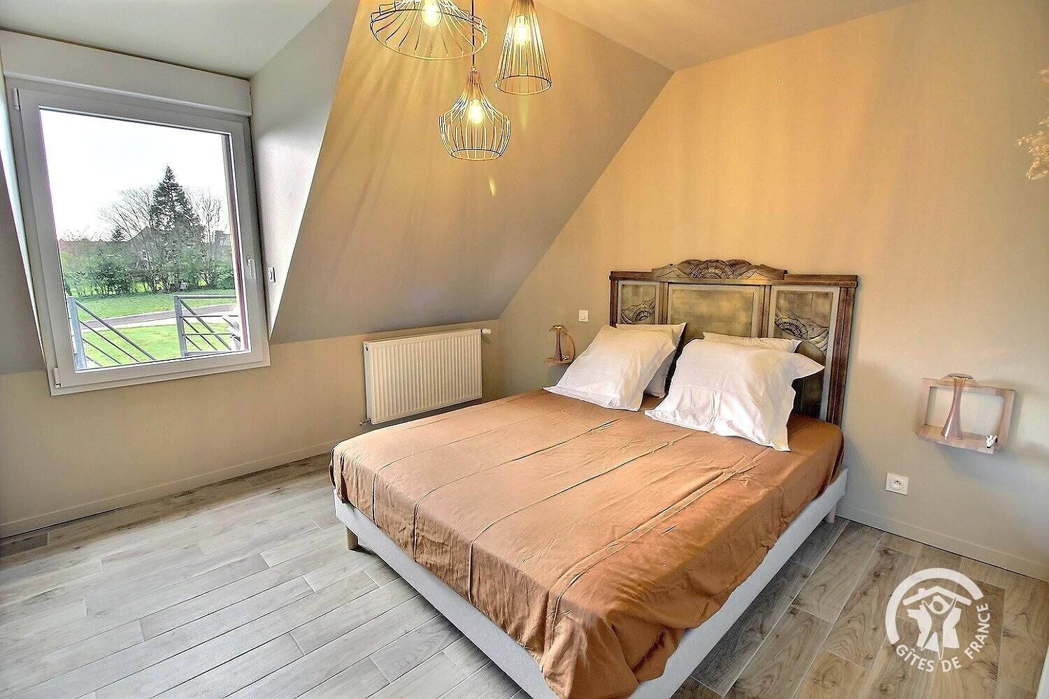 Ein Schlafzimmer mit einem großen Bett, einem Fenster mit Parkblick und einer schrägen Decke mit Pendelleuchten.