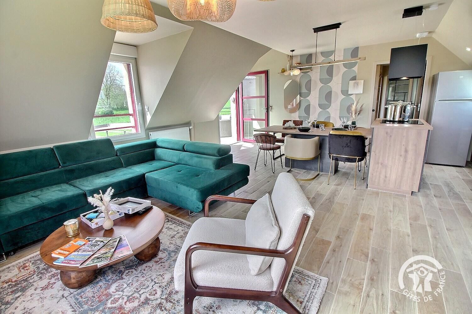 Una sala de estar moderna con un sofá seccional verde, una mesa de centro de madera y un comedor con una cocina al fondo.