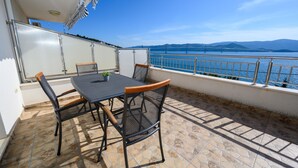 A balcony with a table and chairs, overlooking a body of water and distant mountains.