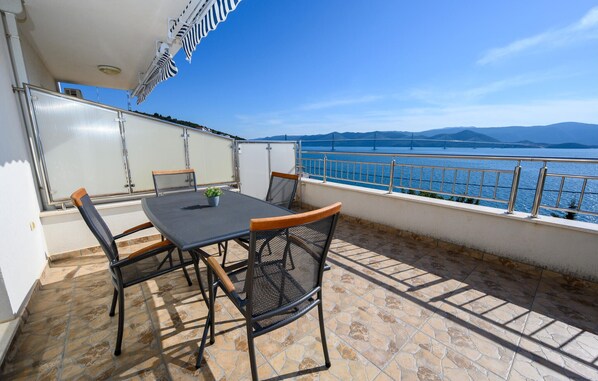 Uma varanda com mesa e cadeiras, com vista para um corpo de água e montanhas ao longe.