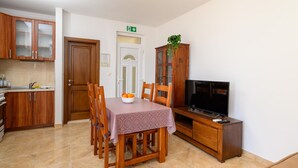 A compact kitchen with wooden cabinets, a dining table with chairs, a television, and a plant.