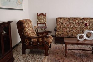 Un salon avec un canapé à motifs, un fauteuil en bois, une table d’appoint agrémentée d’objets décoratifs et un meuble.