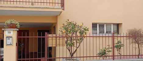 Un edificio residencial con un acceso mediante portón, número 19, y un pequeño árbol en primer plano.