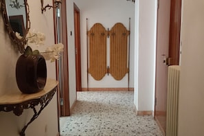 A hallway with a white speckled floor, a mirror, a vase with flowers, and a wooden door with a decorative panel. - SE069 - Senigallia, large four-room apartment convenient to services (Senigallia)