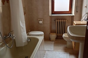 Un baño con bañera, inodoro, lavamanos y ventana.