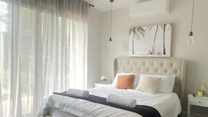 A neatly made bed with white linens, a beige headboard, and a tropical-themed painting above it. - The Grand on Macquarie | Pool & Spa, Ultimate Getaway (Dubbo)