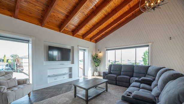 A spacious living room with a large sectional sofa, a flat-screen TV mounted on the wall, and a wooden ceiling. - The Grand on Macquarie | Pool & Spa, Ultimate Getaway (Dubbo)