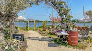 An outdoor seating area with a view of a lake, surrounded by potted plants and a chalkboard sign.
