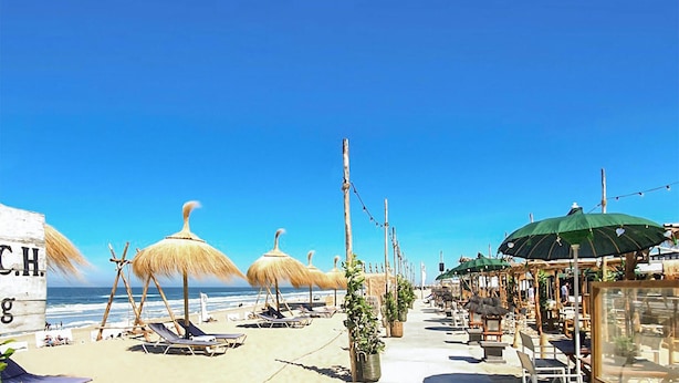 A beachside setting with sun loungers, thatched umbrellas, and a café area with outdoor seating.