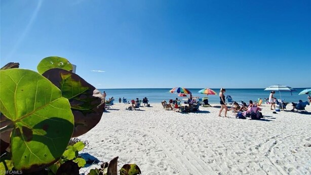 Una playa con gente tomando el sol y paseando, sombrillas y un cielo azul despejado.