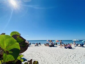 A beach with people sunbathing and walking, umbrellas, and a clear blue sky. - Luxury Beach Retreat Steps from Barefoot Beach & Restaurants (Bonita Springs)