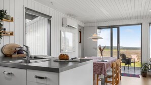 Eine moderne Küche mit großem Fenster, einem Essbereich mit Tisch und Stühlen und Blick ins Grüne.