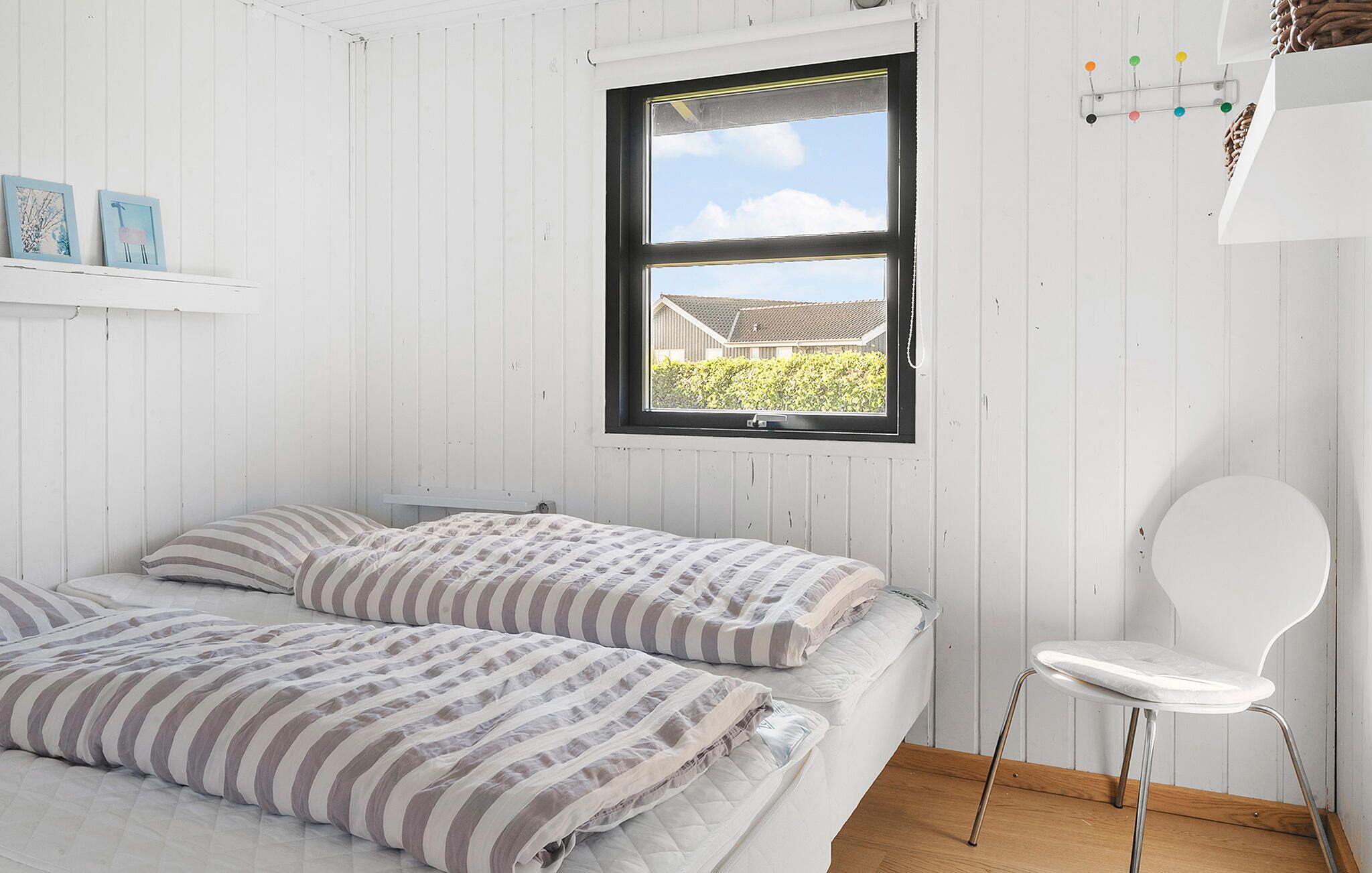Een slaapkamer met een bed, een stoel en een raam met uitzicht op een huis en groen.