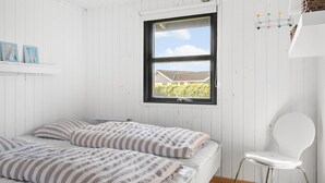 Ein Schlafzimmer mit Bett, Stuhl und Fenster mit Blick auf ein Haus und Grünflächen.