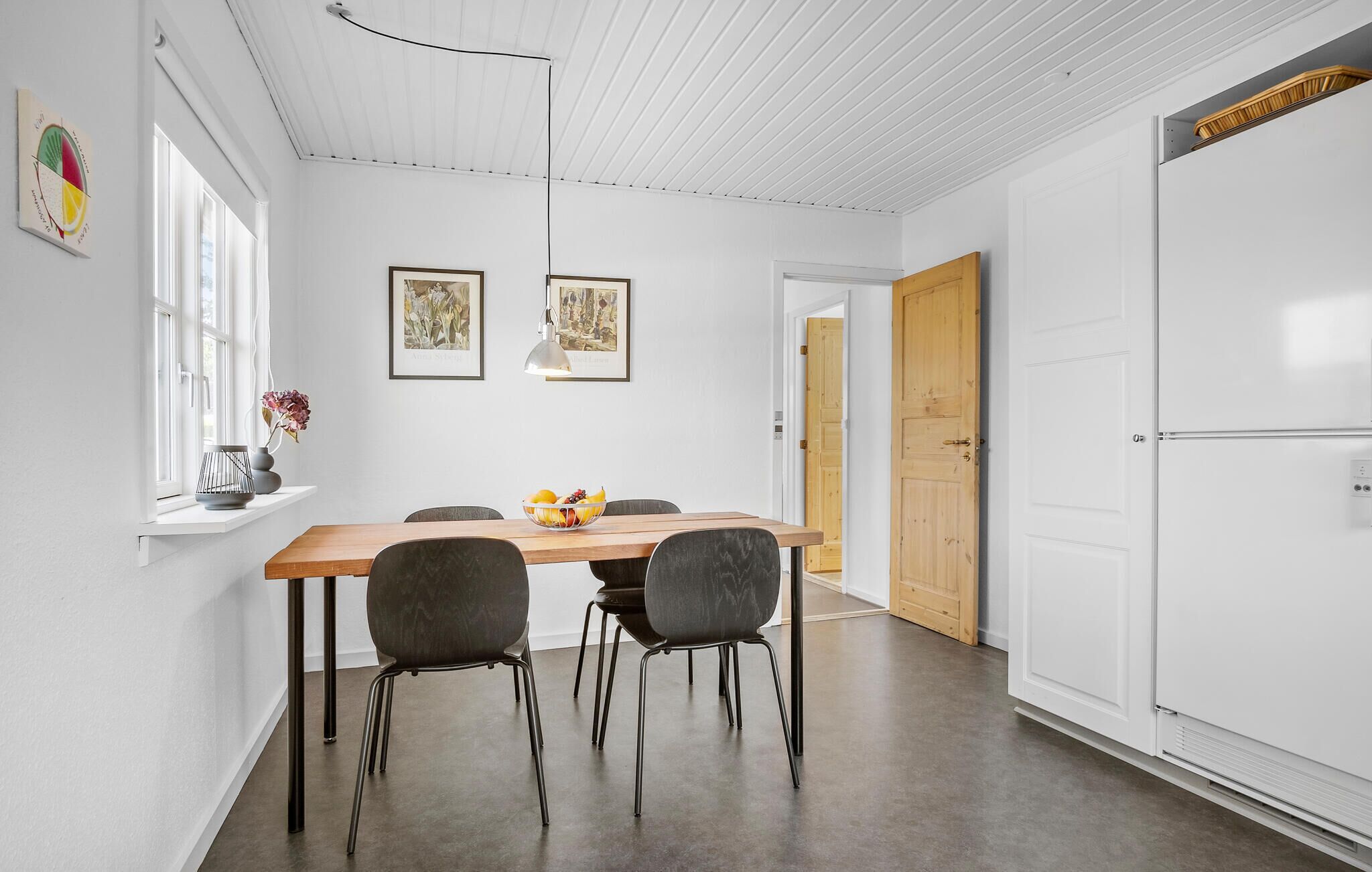A modern dining area with a wooden table, four chairs, and two framed artworks on the wall.