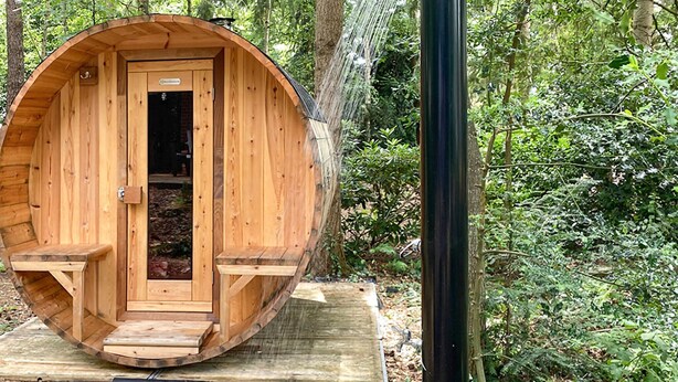 Une cabane en bois avec une porte, un petit porche et un espace douche.