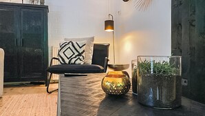 Un salon moderne avec un parquet en bois foncé, un canapé noir agrémenté de coussins à motifs, une table basse en verre, une lampe décorative et une plante en pot.