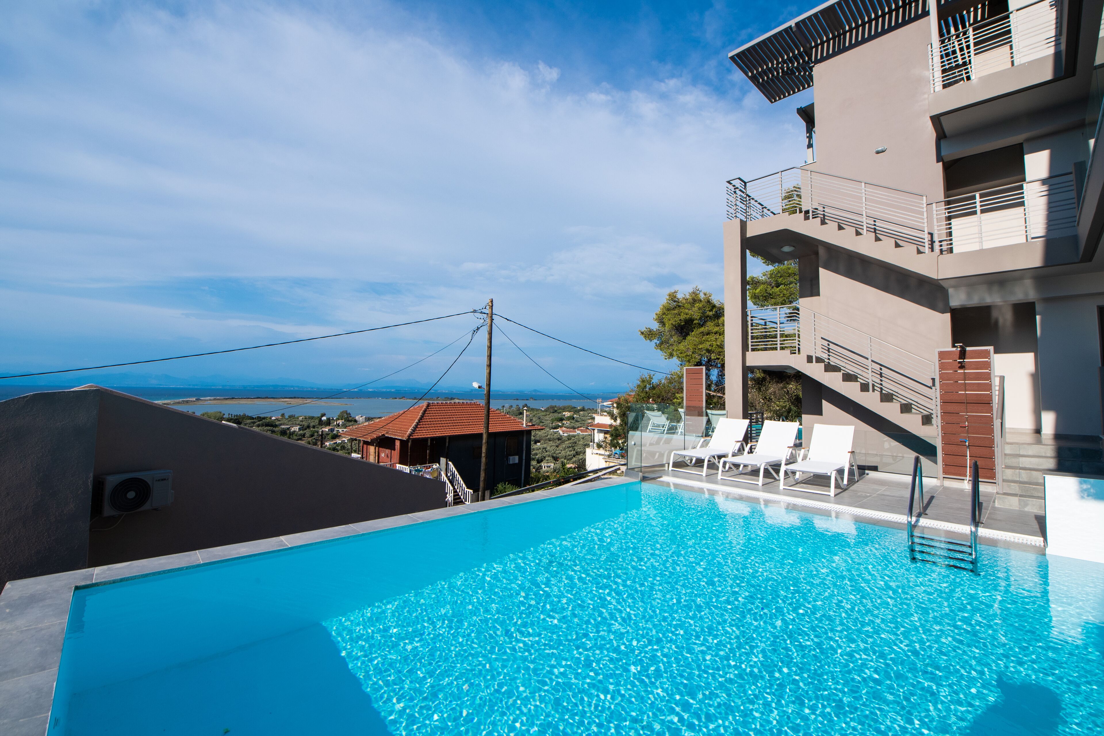 Un hotel moderno con piscina a sfioro sul tetto, vista sul mare e un edificio su due piani con balconi.
