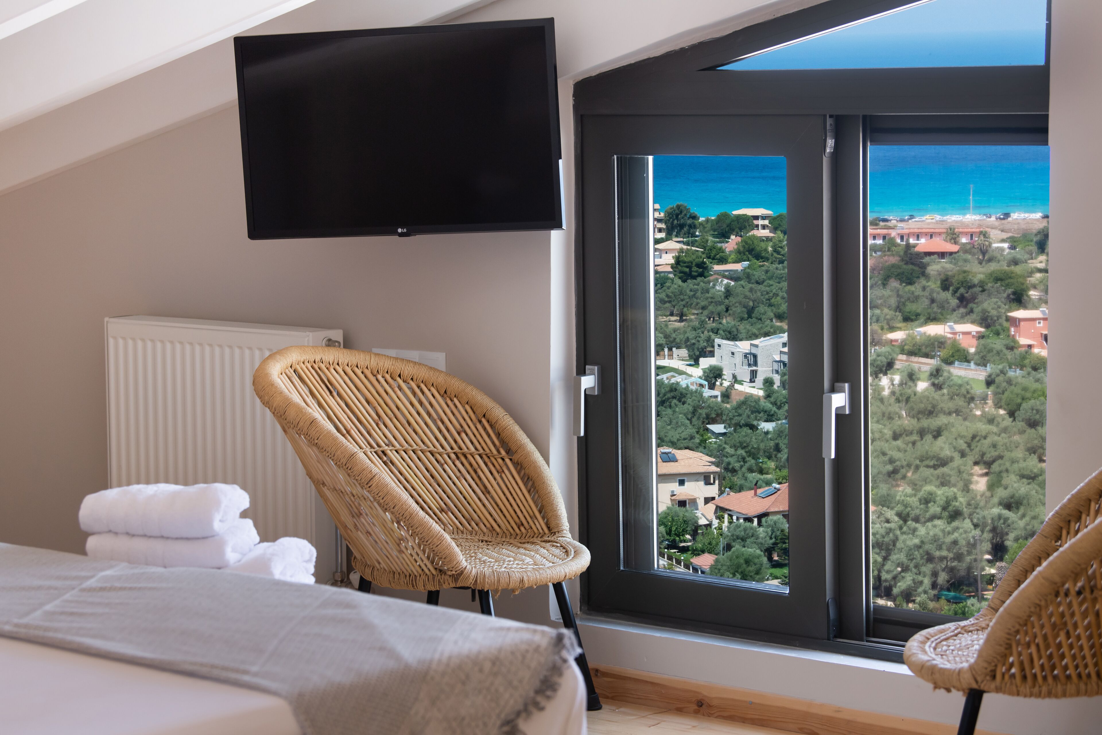 Un dormitorio con un ventanal grande, una cama, un sillón y un televisor de pantalla plana.