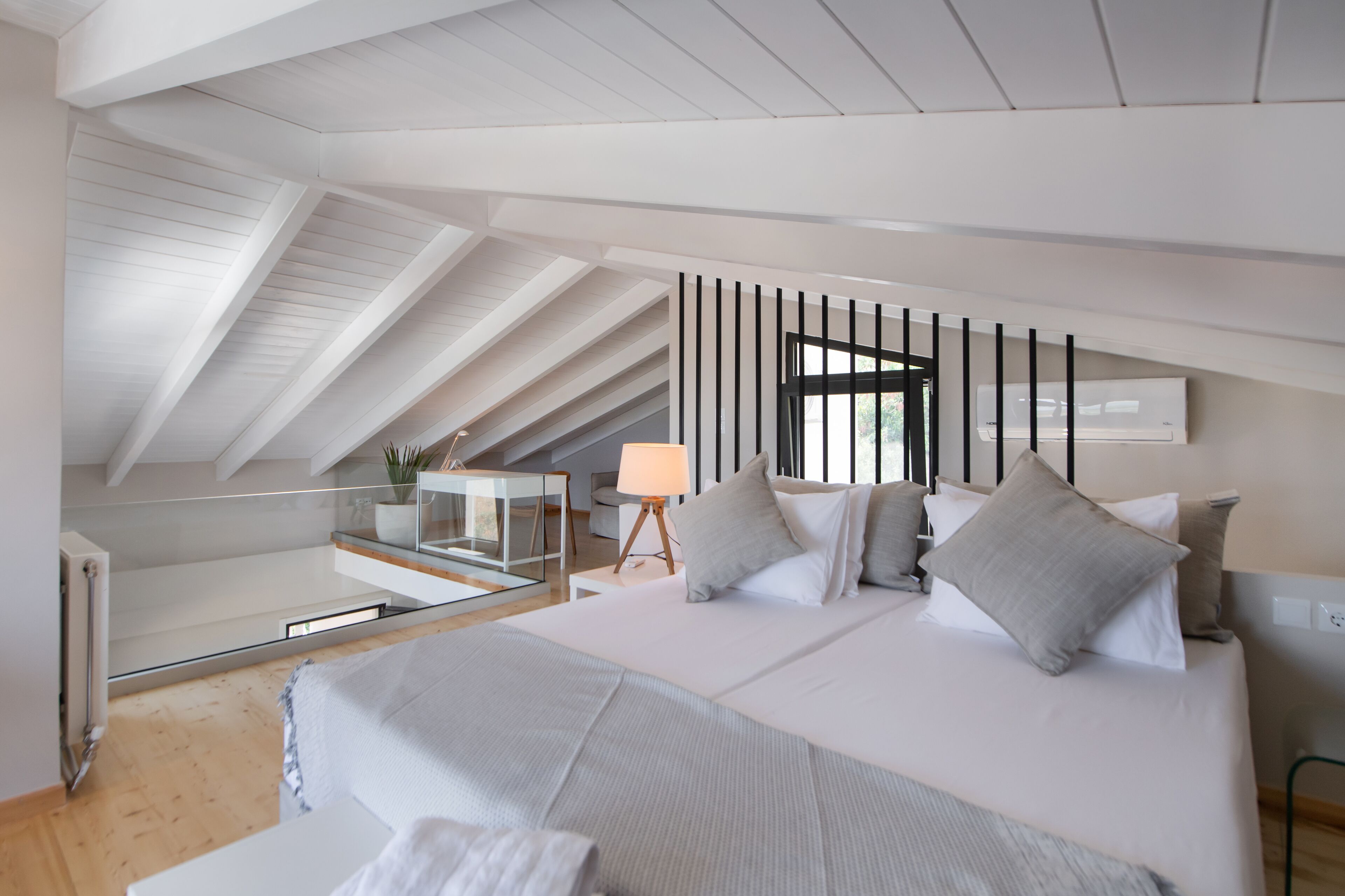 Une chambre moderne avec un grand lit, une table en verre, une lampe et une vue sur l’extérieur.