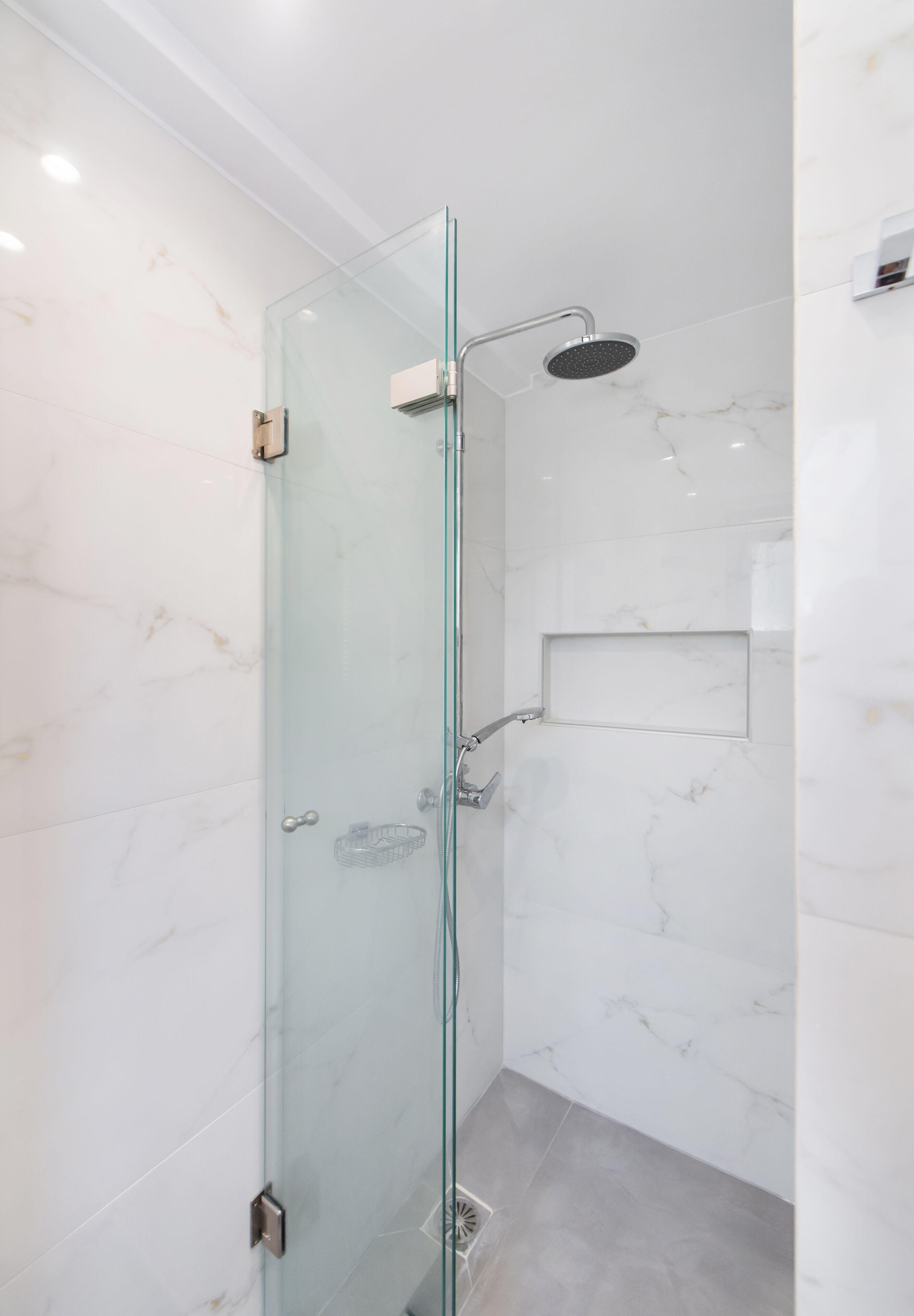 Une douche fermée par des parois de verre, dotée d’un pommeau de douche à main, d’une porte en verre et d’un mur en marbre.