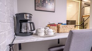 A coffee maker on a white countertop with a coffee mug and a basket of snacks.
